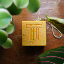 Load image into Gallery viewer, Dragon Fruit, Papaya & Carrot Soap cube surrounded by green leaves on a wooden surface.