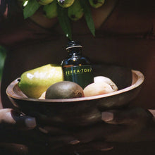 Load image into Gallery viewer, Coriander Seed Omega Body Oil bottle on a wooden bowl filled with fresh fruits and greens.