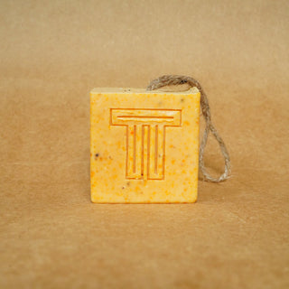 Dragon Fruit, Papaya & Carrot Soap cube with natural fibers on a brown background.