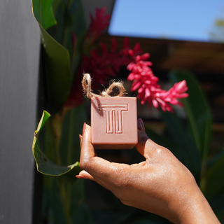 Hand holding a small rectangular object with pink flowers and green leaves in the background