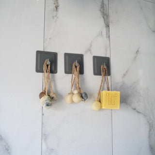 Dragon Fruit, Papaya & Carrot Soap hanging on hooks with decorative clay beads on a marble wall.